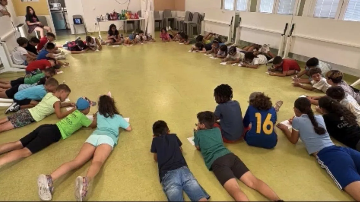 Bambini distesi in cerchio sul pavimento della palestra durante un’attività del centro estivo